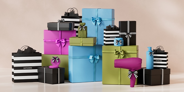 Fond beige neutre sur lequel sont disposés des coffrets-cadeaux et des sacs de magasinage empilés, de couleur bleue, verte, rose et noire, ornés de nœuds en ruban. On y trouve également des sacs rayés de la marque Sephora, ainsi qu’un sèche-cheveux rose po