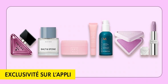 « EXCLUSIVITÉ DE L'APPLICATION » Assortiment d’essentiels beauté comprenant un parfum Prada, un déodorant Salt & Stone, du maquillage Fenty Beauty, un soin Moroccanoil, un fard à joues et un rouge à lèvres, le tout sur fond lavande.
