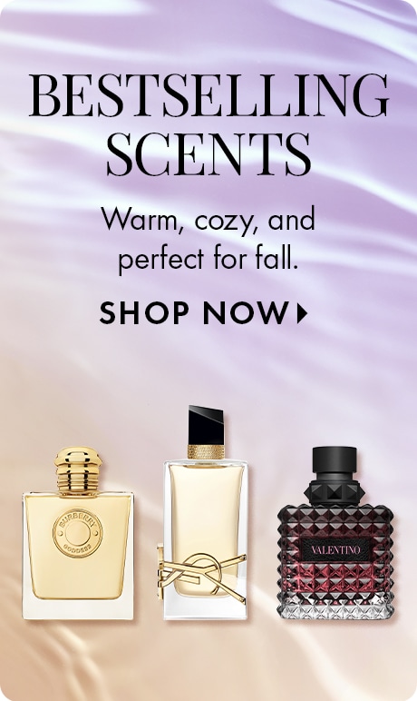 Three perfume bottles are displayed with the text: “Warm, cozy, and perfect for fall. SHOP NOW.” The bottles include a gold-capped square design, a rectangular bottle with black and gold accents, and a textured red bottle labeled “VALENTINO.”