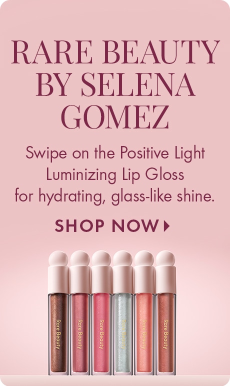 Image featuring Rare Beauty by Selena Gomez with text: “Swipe on the Positive Light Luminizing Lip Gloss for hydrating, glass-like shine. SHOP NOW.” Shows six lip gloss tubes in various shades arranged in a row.