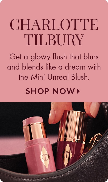 Dusty pink background with text reading “Charlotte Tilbury” and “Get a glowy flush that blurs and blends like a dream with the Mini Unreal Blush,” plus “Shop Now.” Two Charlotte Tilbury blush sticks are shown inside an open black bag.