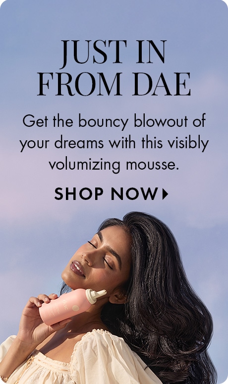 Blue gradient background with text reading “Just In From dae” and “Get the bouncy blowout of your dreams with this visibly volumizing mousse: Shop Now.” A person holds a pink dae mousse bottle, with long hair flowing across the lower half of the image.