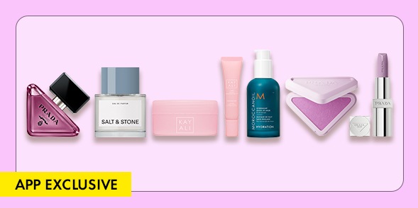 "APP EXCLUSIVE" Assorted beauty products including Prada fragrance, Salt & Stone deodorant, Fenty Beauty makeup, Moroccanoil treatment, blush, and lipstick on a lavender background.