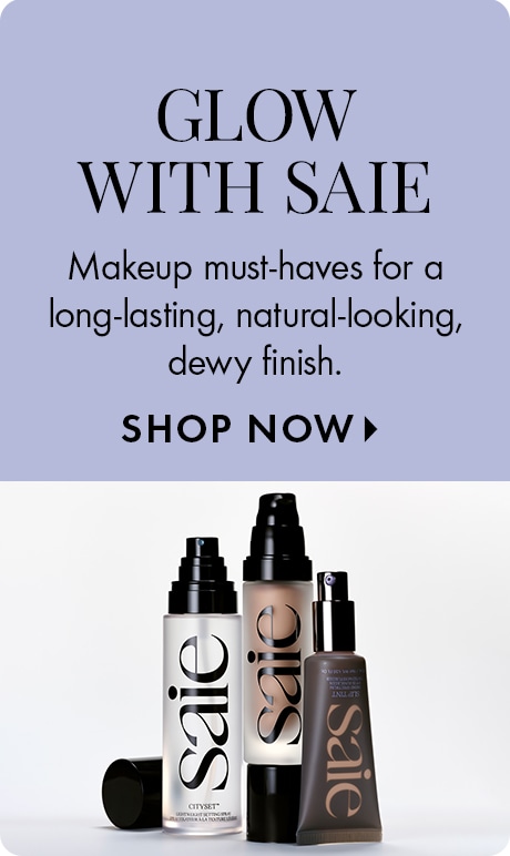 Text on a light lavender background reads: “Glow with Saie. Makeup must-haves for a long-lasting, natural-looking, dewy finish. Shop Now.” Below are three Saie products in sleek black and white packaging, including foundation and highlighter bottles.