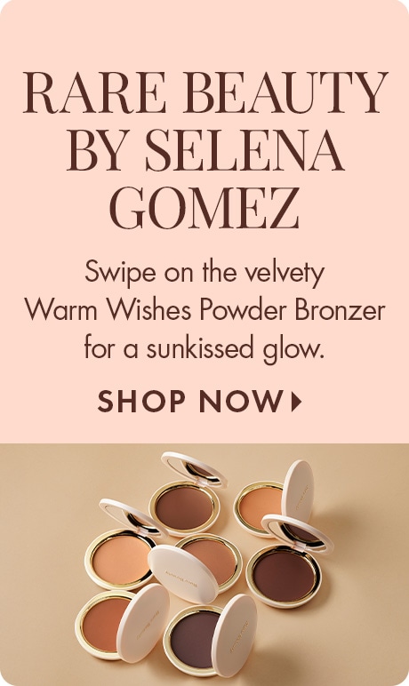 Text on a blush background reads: “Rare Beauty by Selena Gomez. Swipe on the velvety Warm Wishes Powder Bronzer for a sunkissed glow. Shop Now.” Below are open compact bronzers in multiple shades arranged on a beige surface.