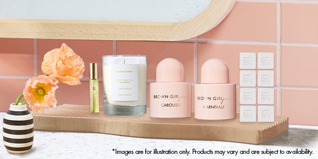 Brown Girl Jane beauty set with candle and perfume on a wooden shelf beside a striped vase with flowers.