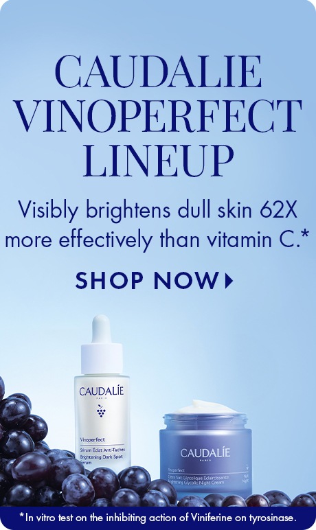 Light blue background with text reading “Caudalie Vinoperfect Lineup.” Below: “Visibly brightens dull skin 62X more effectively than vitamin C,” with “Shop Now.” A Vinoperfect serum bottle and cream jar sit among dark grapes.
