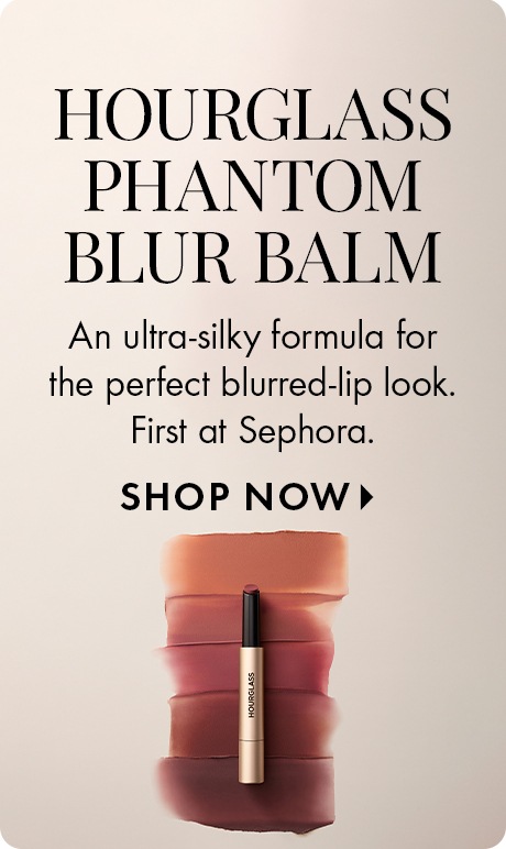 Neutral beige background with text reading “Hourglass Phantom Blur Balm” and “An ultra‑silky formula for the perfect blurred‑lip look. First at Sephora,” plus “Shop Now.” A lip balm tube appears centered over stacked swatches of nude and rose shades.