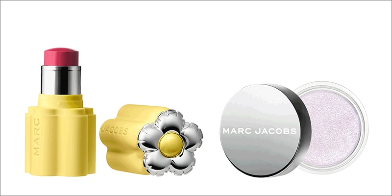 Close-up product image on light background: bold pink lipstick in a sculpted yellow Marc Jacobs tube with silver detail, next to a silver daisy-shaped cap, and a round pot of shimmery pale pink eyeshadow.