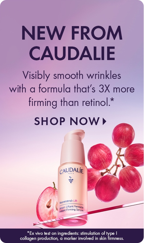 "NEW FROM CAUDALIE" Text: “Visibly smooth wrinkles with a formula that’s 3X more firming than retinol.*” “SHOP NOW.” Pink Caudalie Resveratrol-Lift serum bottle with red grapes and a sliced grape on a pink-to-purple gradient background.
