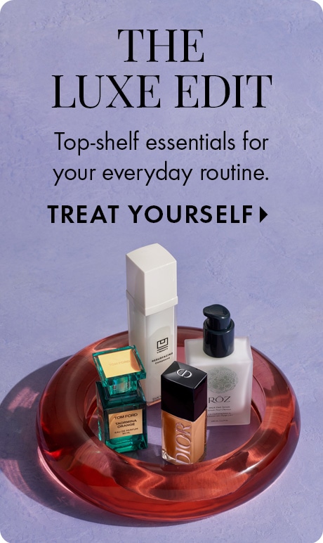 Lavender textured background with text reading “The Luxe Edit,” “Top‑shelf essentials for your everyday routine,” and “Treat Yourself.” Below, luxury beauty products sit on a translucent red tray, including fragrance, makeup, skincare, and hair items.